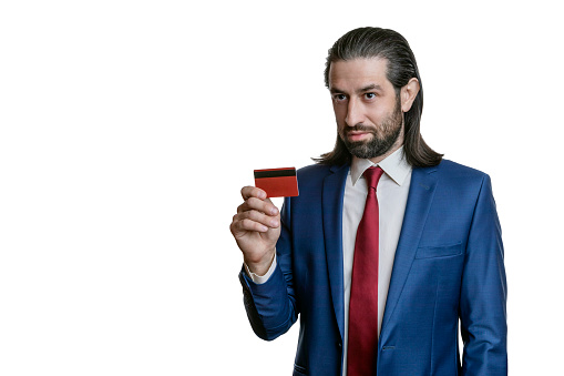 Charismatic businessman with a beard and long hair in a blue jacket and red tie with credit cards in his hand isolated on a white background. Portrait of an office worker.