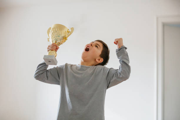 niño imaginando éxito, levantando los brazos con trofeo de oro y gritando - winning achievement award little boys fotografías e imágenes de stock
