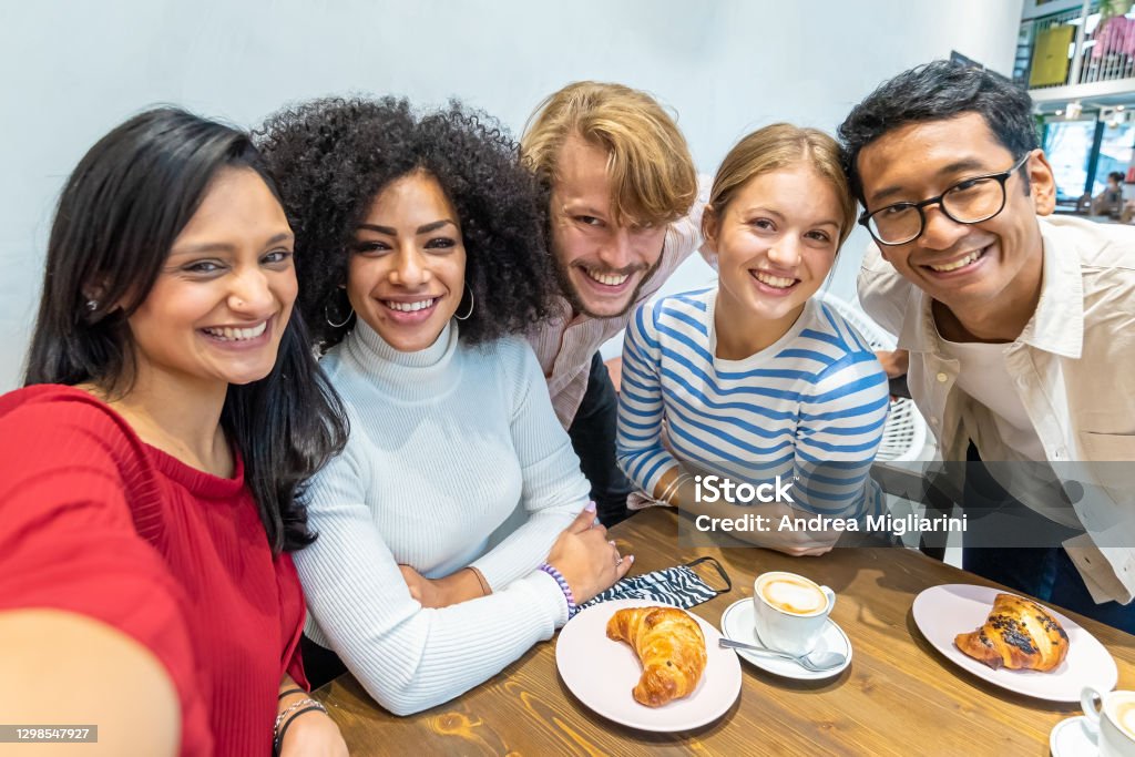 smiling friends take a selfie during breakfast, multi-ethnic university Erasmus group in a moment of rest and coffee takes a souvenir photo, concept of resumption of sociality after the epidemic Friendship Stock Photo