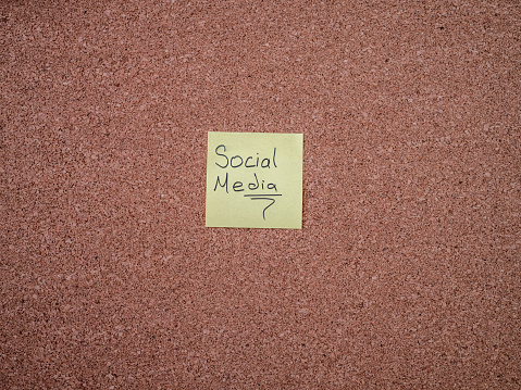 Yellow sticky note with social media handwritten on cork board