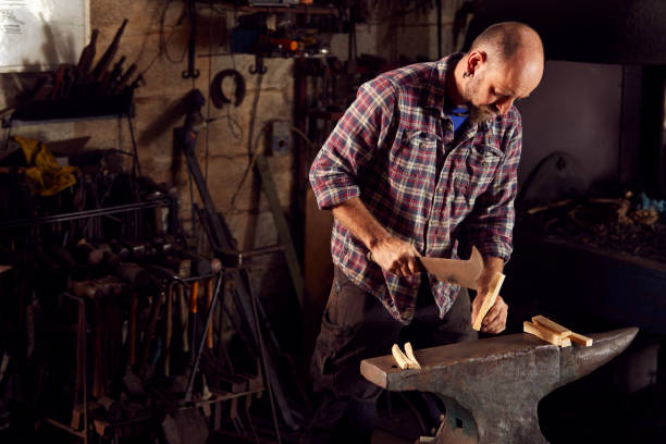 istock Male Blacksmith Chopping Wood For Kindling On Anvil To Light Forge 1298555048