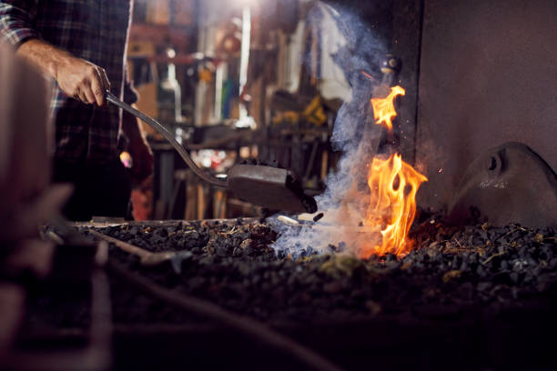 istock Male Blacksmith Adding Coal Fuel To Wood Kindling To Start Blaze In Forge 1298555135