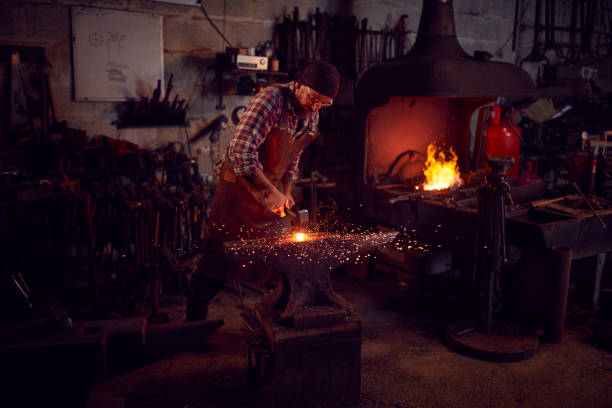istock Male Blacksmith Hammering Metalwork On Anvil With Blazing Forge In Background 1298556285