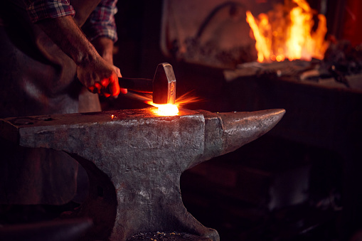 Shot of a blacksmith working with a hot metal rod in a foundry