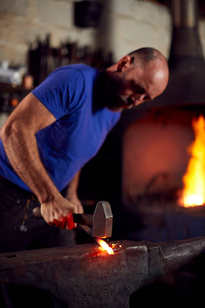 istock Male Blacksmith Hammering Metalwork On Anvil With Blazing Forge In Background 1298556551