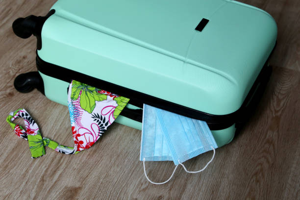 istock Suitcase with swimsuit and protective face masks on the floor 1298561515