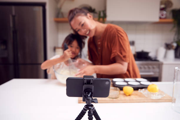 istock Asian Mother And Daughter Baking Cupcakes In Kitchen At Home Whilst On Vlogging On Mobile Phone 1298561802