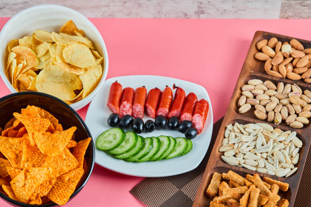 istock Assorted snacks on the pink table. Chips, sausages, pistachios, olives 1298562909