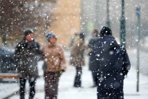 Pedestrians in the city during a severe blizzard. Persons crossing the street, snow storm. Focus on foreground snowflakes