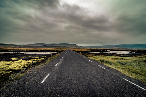 Scenic countryside road through the grasslands, stretching towards the fog at the  horizon in rural Iceland.