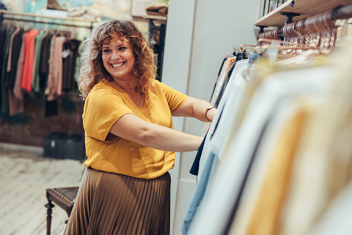 Woman working in a clothing shop. Female owner looking away and smiling while helping a customer to buy in a fashion store.