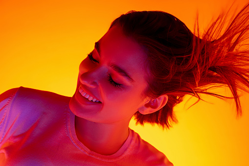 Caucasian woman's portrait isolated on orange studio background in multicolored neon light