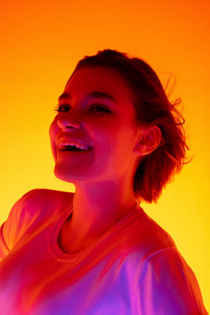 istock Caucasian woman's portrait isolated on orange studio background in multicolored neon light 1298572471