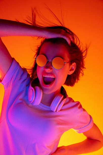 istock Caucasian woman's portrait isolated on orange studio background in multicolored neon light 1298572472