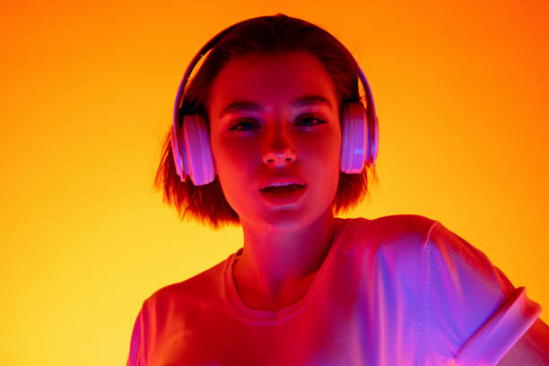 istock Caucasian woman's portrait isolated on orange studio background in multicolored neon light 1298572475