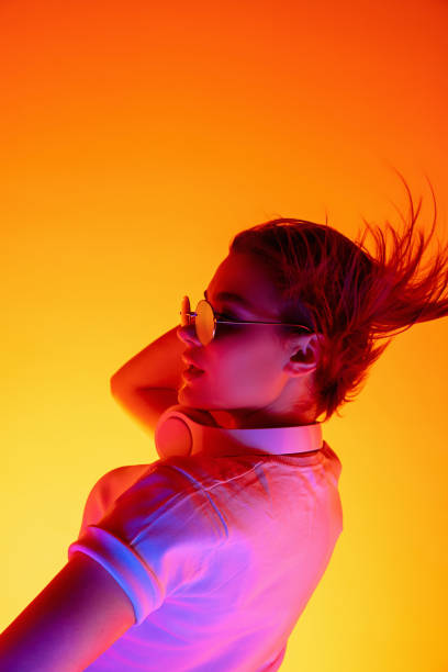 istock Caucasian woman's portrait isolated on orange studio background in multicolored neon light 1298572480