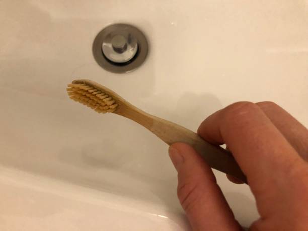 istock Hand holds bamboo toothbrush over sink 1298574229