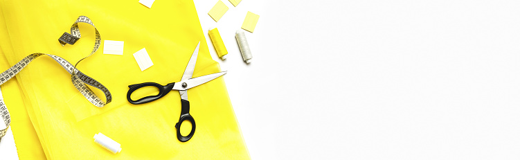 The trendy color of 2021. Tailoring concept. beautiful yellow fabric with sewing thread, scissors, tape measure, chalk and spool on a white background. Top view. Flat lay. Banner