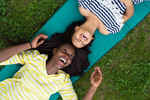Young smiling mother lying on exercise mat with her daughter on grass field, directly above