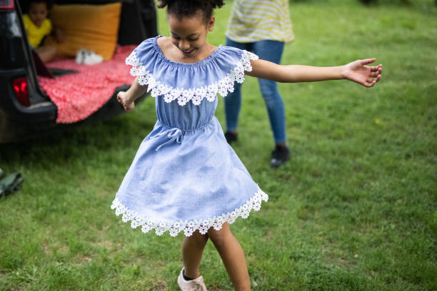 Young smiling girl in dress standing on grass field and spinning around