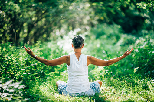 Inner peace meditation. Mindful woman meditating with open arms, sitting on the ground, surrounded by beautiful nature nurturing and increasing sense of inner peace