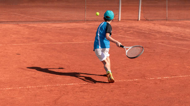 테니스 코트에 아이. 소년 테니스 선수는 포핸드를 공격하는 법을 배움. 아이들의 신체 활동과 스포츠 교육. 학교 나 클럽에서 테니스 훈련. 배경, 복사 공간 - tennis forehand people sports and fitness 뉴스 사진 이미지