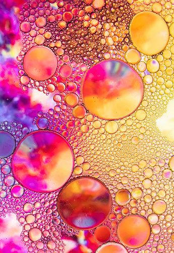 abstract photograph of oil and soap bubbles with yellow, blue, pink and red colors, in a glass bowl with water