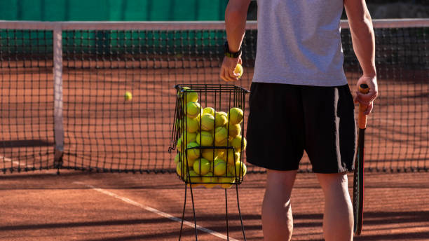 Tennis coach conducts training on red clay court, basket with tennis balls near him. Blurred background. Sports activity and leisure concept. Lifestyle Tennis coach conducts training on red clay court, basket with tennis balls near him. Blurred background. Sports activity and leisure concept. Lifestyle tennis coach stock pictures, royalty-free photos & images