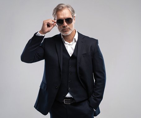 Portrait of a respectable mature man in a suit and sunglasses on a gray background. Businessman portrait. Copy space.