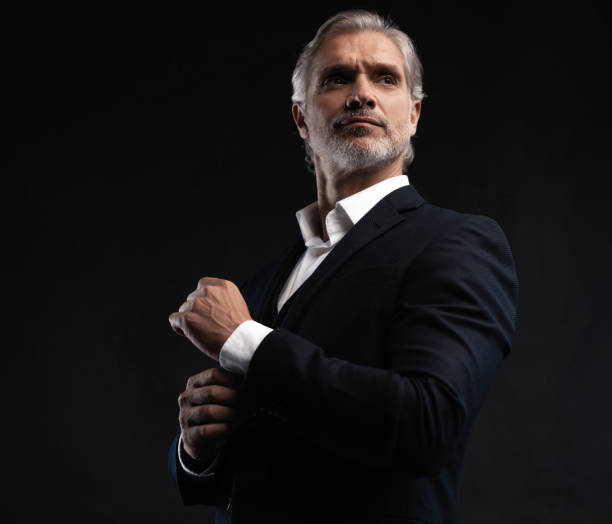 istock Handsome middle-aged man in suit posing against black background 1298586746