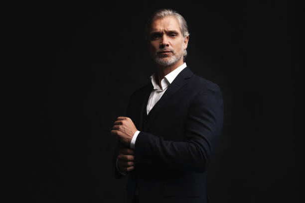 istock Handsome middle-aged man in suit posing against black background 1298586748