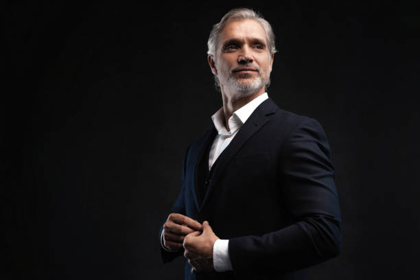 istock Handsome middle-aged man in suit posing against black background 1298586753