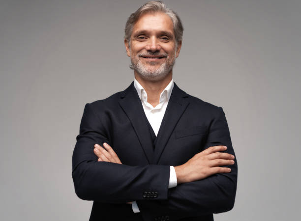 istock Handsome smiling middle-aged man in suit posing against grey background 1298587951