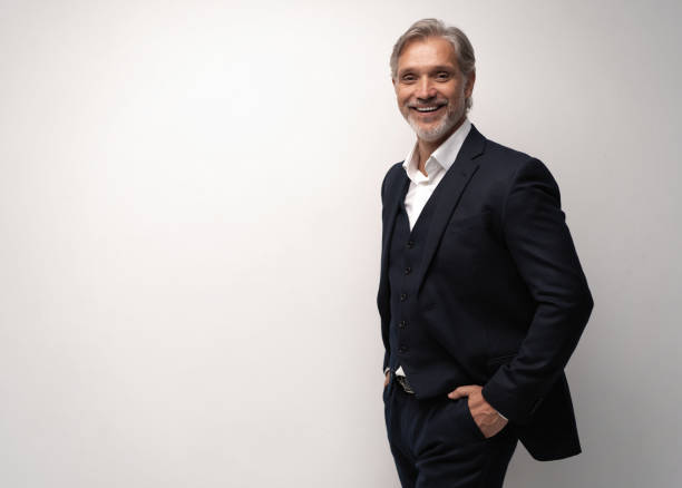 istock Handsome smiling middle-aged man in suit posing against grey background 1298587984