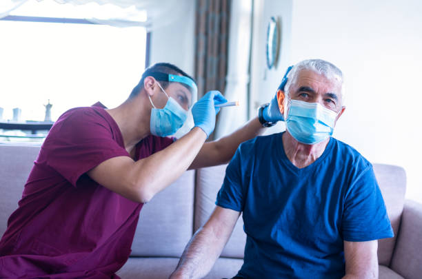 l’agent de santé masculin examine l’oreille de l’homme aîné dans sa maison pendant l’épidémie de coronavirus. soins à domicile - vertige photos et images de collection