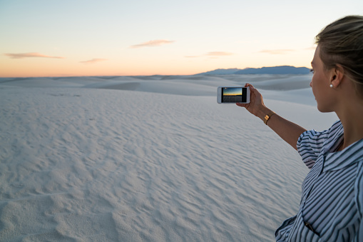 Crop hiker using smartphone and taking photo of sandy dune and enjoying sunset while exploring desert in White Sands National Park