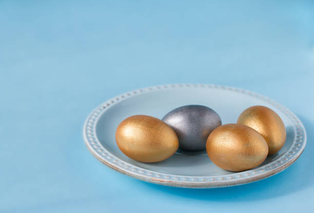 istock Golden and silver Easter eggs on a porcelain saucer on a blue background. Front view. 1298607756