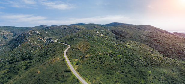 Empty long mountain road to the horizon on a sunny summer day at bright sunset - aerial drone shot.