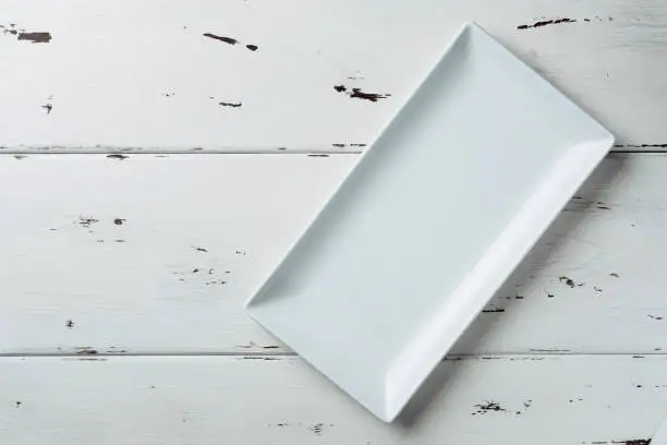 Photo of Top view of a white rectangular plate on a white wooden background.