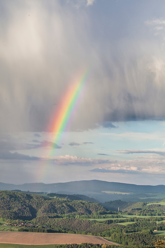 Distant view of Ambronay small village with famous abbey and with beautiful rainbow due to stormy bad weather. This image was taken in Bugey, Alps mountains near Jura massif, in Ain, Auvergne-Rhone-Alpes region in France.