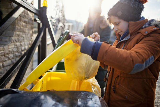 Children taking out garbage on the winter day. The boy is throwing plastic waste to yellow plastic garbage bin. The girl is throwing out glass to green bin.\nShot with Canon R5