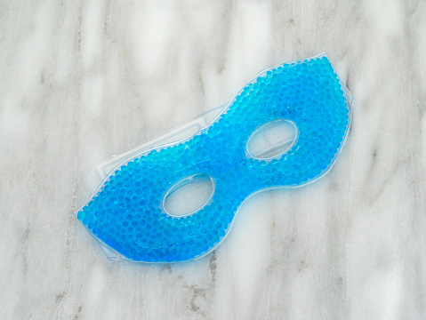 A blue beaded gel eye mask at an angle atop a marble counter top.