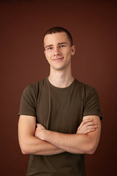 Studio portrait of 18 year old man Close up studio portrait of 18 year old man with short brown hair in green khaki t-shirt on brown background olive green shirt stock pictures, royalty-free photos & images