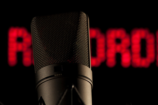 Detail of a microphone in a darkened studio in front of a red glowing lettering