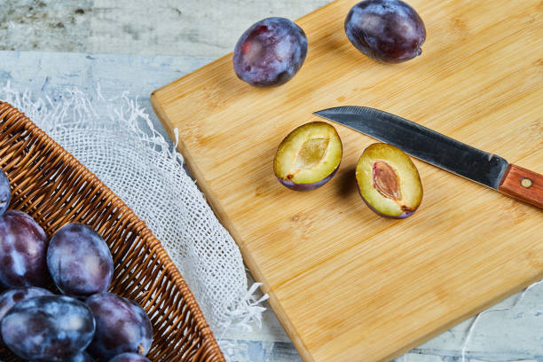 Basket of fresh plums with knife and cutting board on blue table, close up