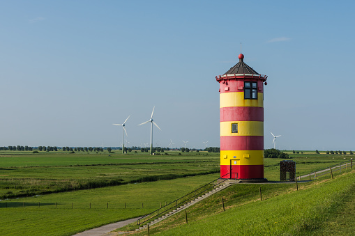 Pilsum Lighthouse on a dike with wind turbines in background. The Pilsum Lighthouse was built in 1891 and is located near the East Frisian village of Greetsiel on the German North Sea coast.