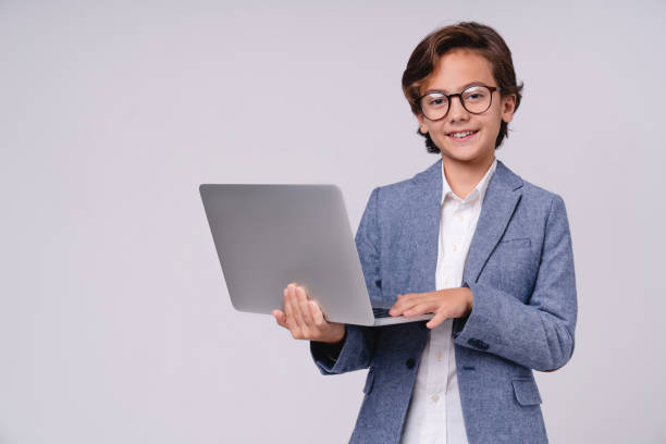 istock Smart little boy with laptop in formal clothes isolated over grey background 1298622405