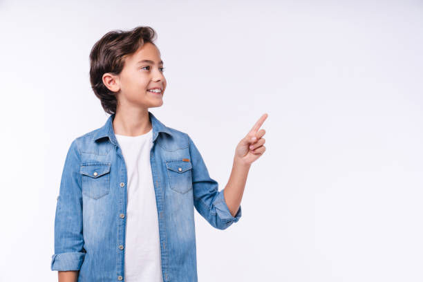 side view portrait of young 10s boy in casual outfit pointing at copy space isolated over white background - schoolboy relaxation happiness confidence imagens e fotografias de stock