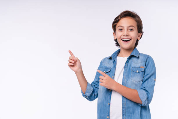 amazed young male kid pointing at copy space isolated over white background - schoolboy relaxation happiness confidence imagens e fotografias de stock