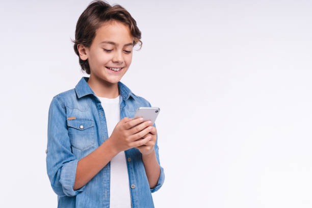 istock Excited small kid with a mobile phone isolated over white background 1298623289